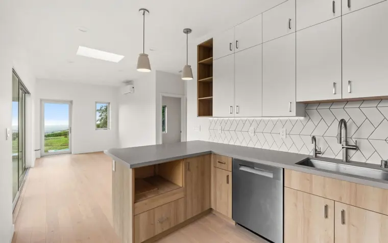 Finished open-concept kitchen with skylight and pendant lights, opening to a hallway with sliding glass doors and hillside view