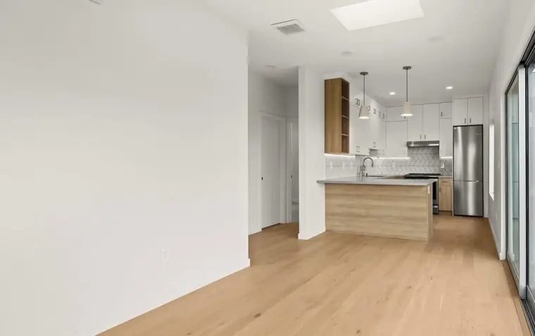Open-concept interior view from empty living area toward finished kitchen with white cabinets, wood island, and stainless appliances