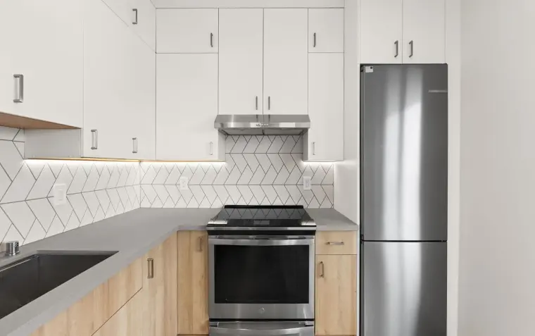 Close-up of finished kitchen range hood, herringbone tile backsplash, and stainless refrigerator