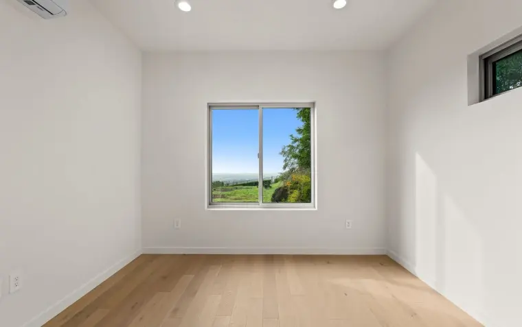 Finished empty bedroom with single window framing hillside view and ceiling-mounted mini-split AC