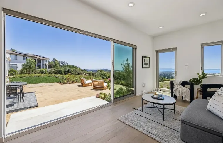 Living room with a wide sliding glass door opening to a patio and bay view, gray sofa, and round coffee table on oak floor