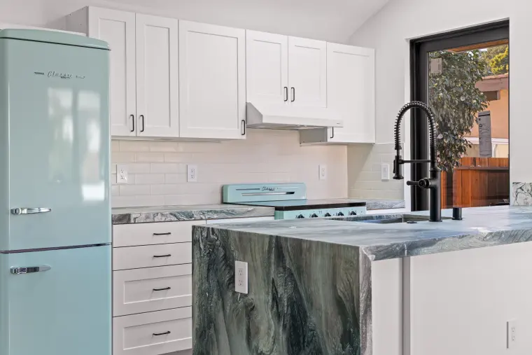Mint retro refrigerator beside white shaker cabinets, subway tile, and a green-veined stone waterfall island with black faucet