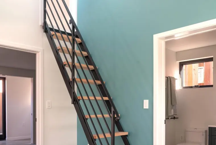 Loft staircase with black metal railing and wood treads against a teal accent wall, bathroom doorway visible alongside
