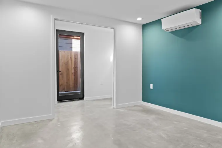 Room with polished concrete floor, a teal accent wall with mini-split, and a black-framed glass door to the side yard