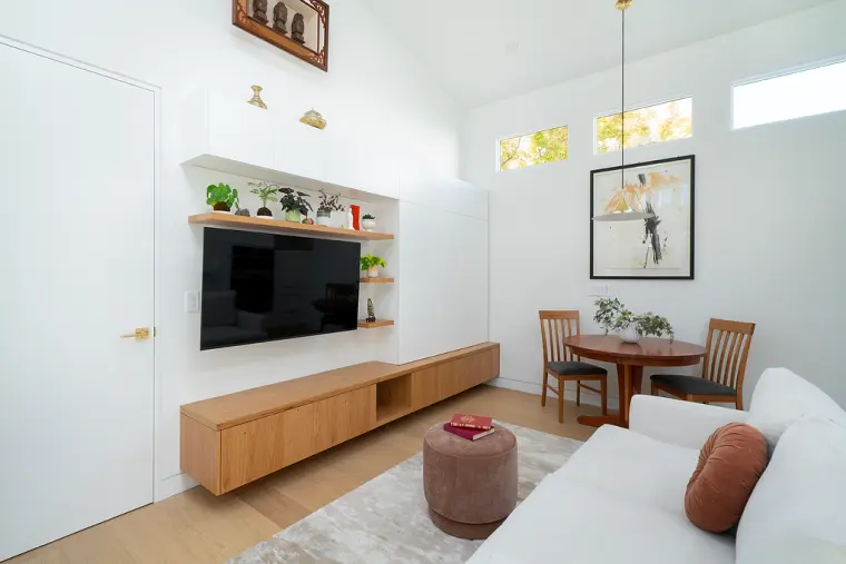 Media wall with open oak shelves around the TV and a floating oak console, with clerestory windows above the dining spot