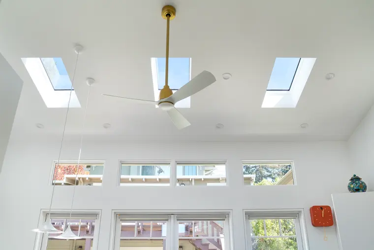Vaulted ceiling with three skylights, a white and brass ceiling fan, and a row of clerestory windows above the doors
