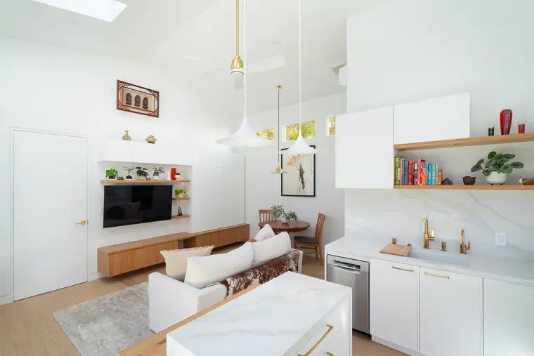 Kitchen and living area from above the waterfall island, with open oak shelves, a full-height slab backsplash, and the media wall beyond