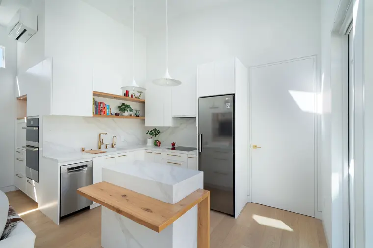 Kitchen with white slab cabinets, a stainless refrigerator, and a waterfall island wrapped with a white oak ledge