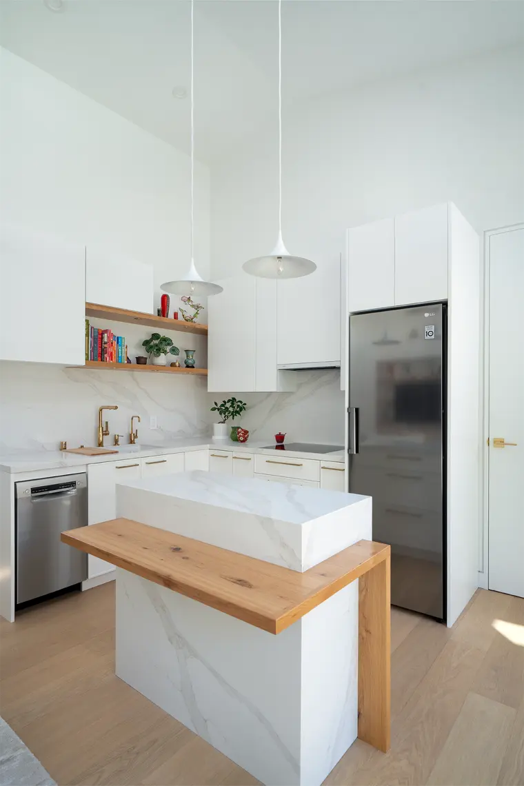 Waterfall island with an oak ledge in front of white cabinets, open oak shelves, and white cone pendants