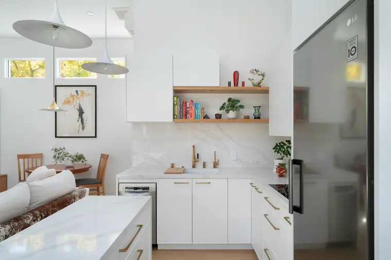 L-shaped kitchen with brass pulls, open oak shelves, and a veined slab backsplash, the dining spot past the island