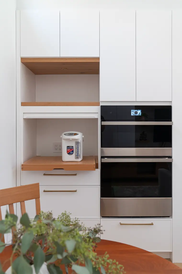 Tall white cabinet wall with a double wall oven and an open oak-lined appliance nook