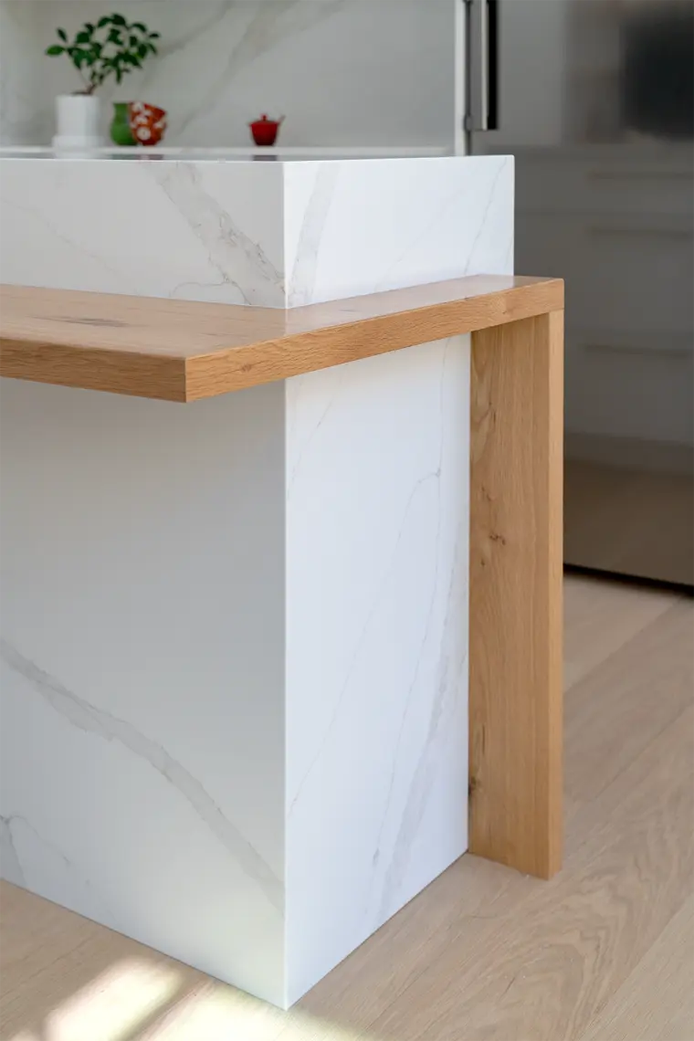 Detail of the waterfall island where the white oak ledge wraps the veined slab end