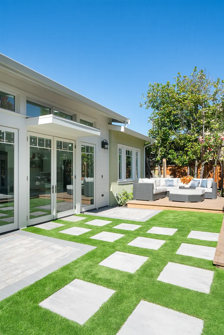 The ADU from a corner, with two sets of French doors, a paver patio, and turf with stepping pads leading to a lounge deck