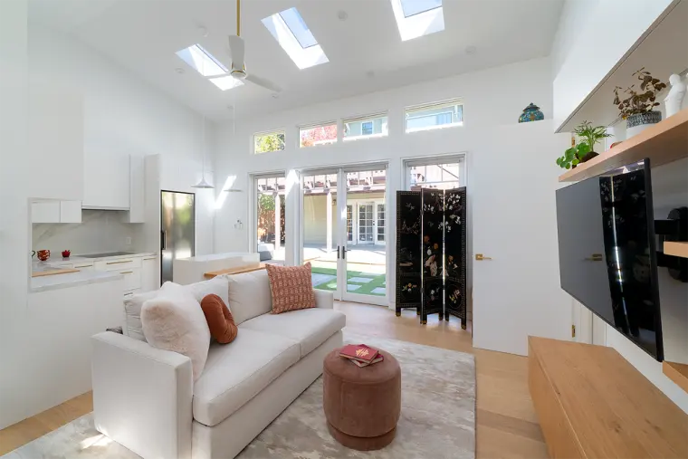 Great room looking toward the French doors, with three skylights, a ceiling fan, a cream sofa, and a floating oak media console