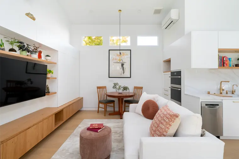 Living area with a built-in media wall and oak console, the dining table under a brass pendant, and the kitchen beyond