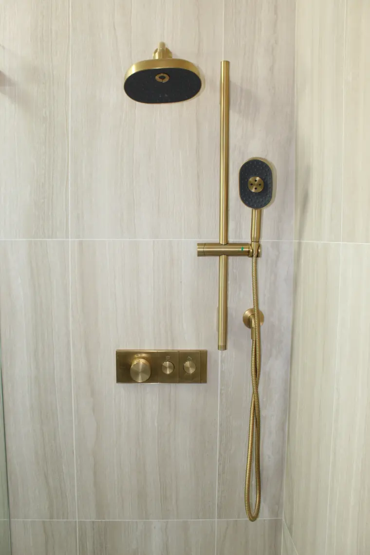 Shower wall of large wood-look porcelain tile with a brushed brass rain head, handheld shower on a slide bar, and brass valve trim