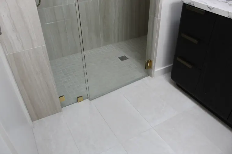 Curbless shower entry with a glass panel, small square floor tile, square drain, and large-format light floor tile
