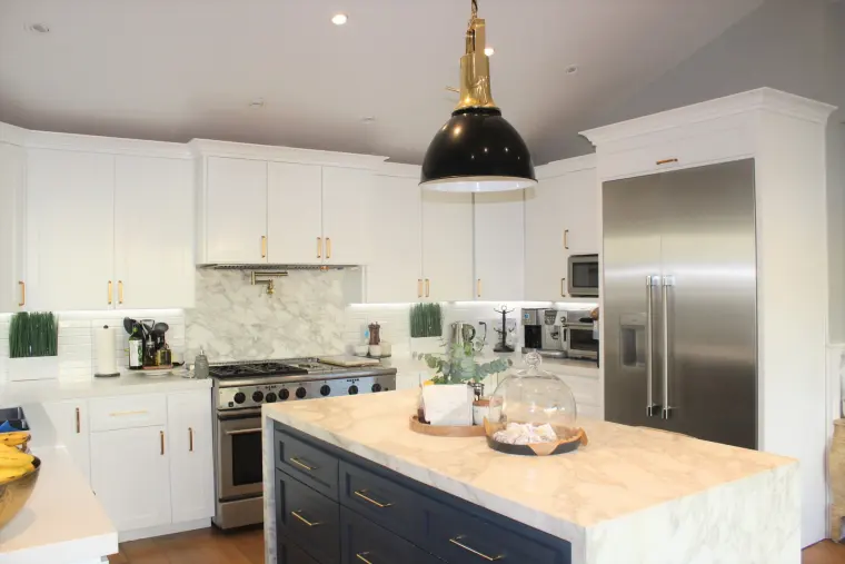 White kitchen with a navy island, marble waterfall counter, and a black and brass pendant