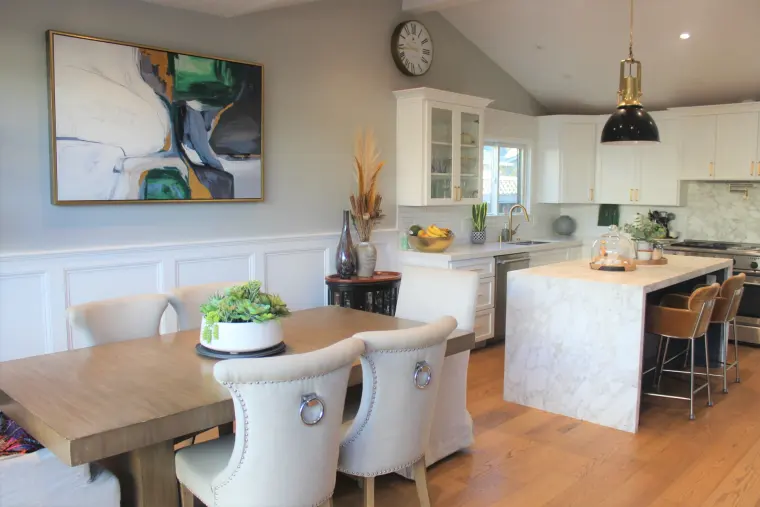 Dining area and kitchen under a vaulted ceiling with white wainscoting on the walls