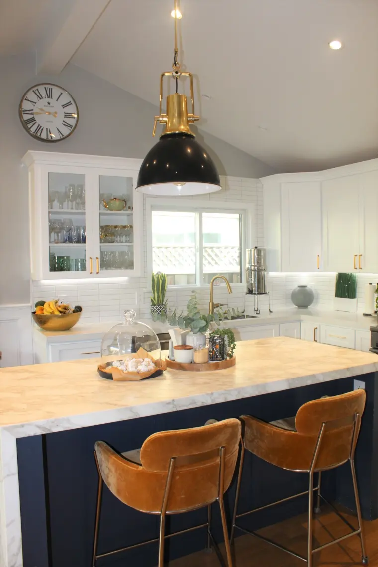 Navy island with a marble top and leather stools, glass-front cabinets behind