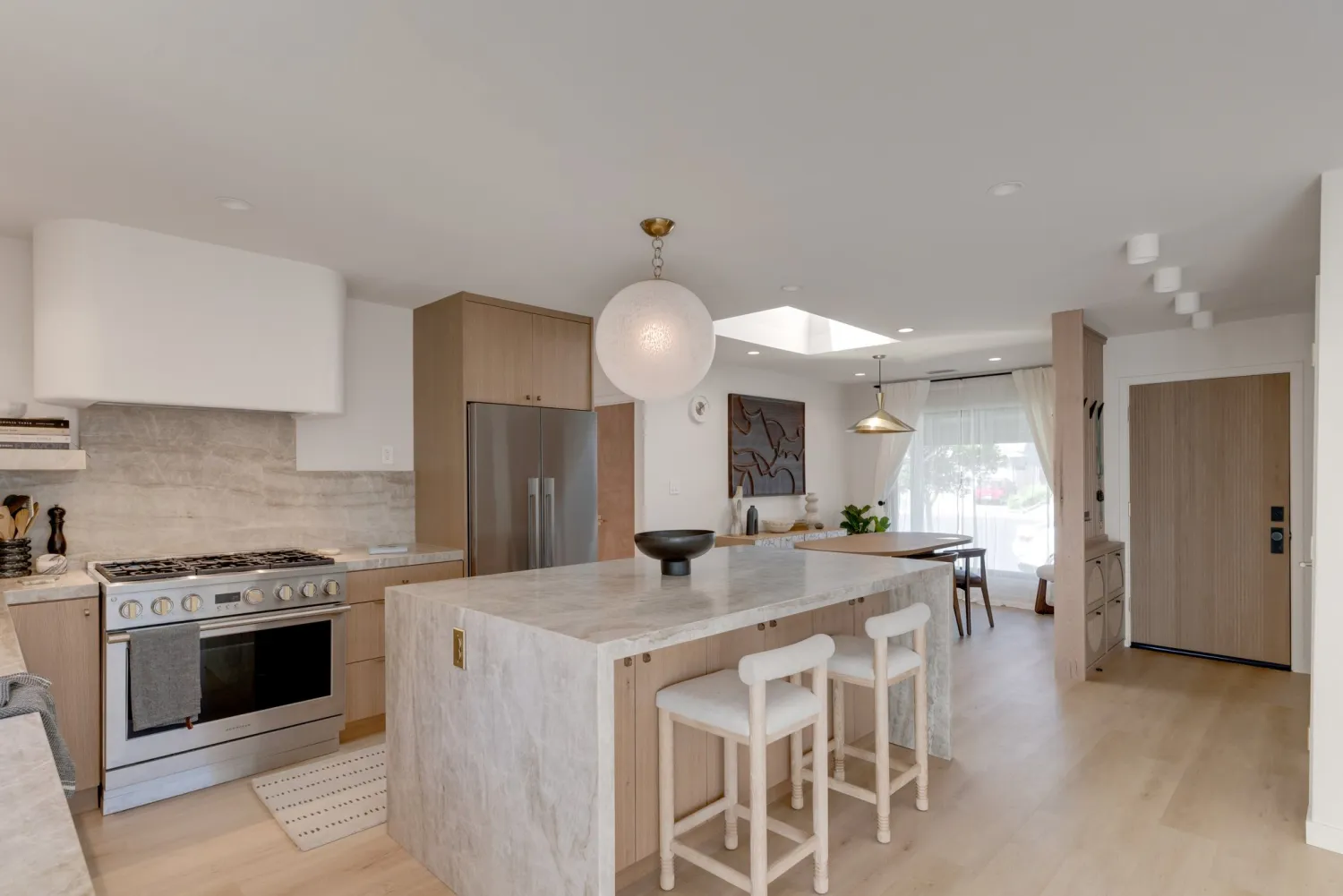 Open kitchen and living area with a stone waterfall island, globe pendant, pale oak floors, and a professional range