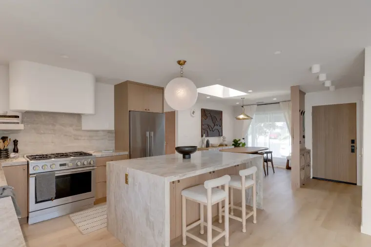 Open kitchen and living area with a stone waterfall island, globe pendant, pale oak floors, and a professional range