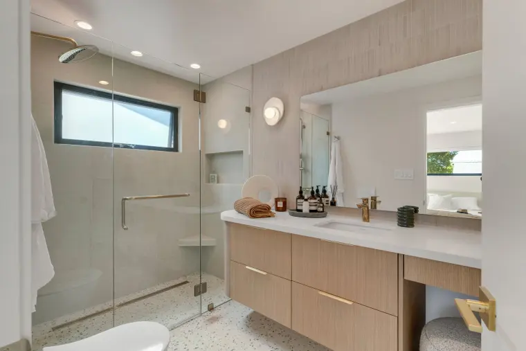 Bathroom with a frameless glass shower, pale oak vanity, and a black-framed window