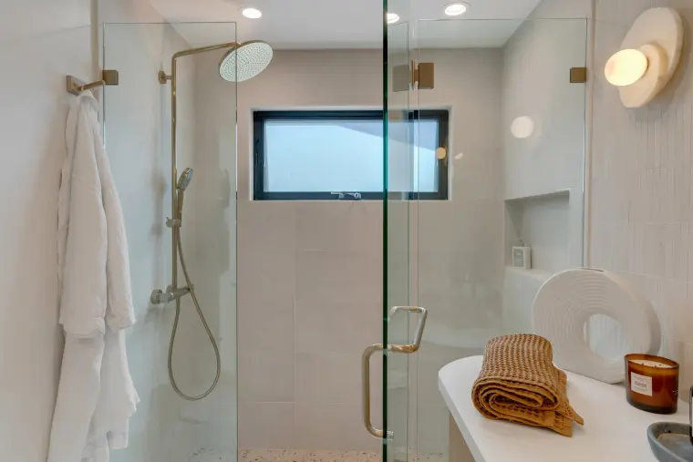 Frameless glass shower with brushed brass fixtures, a built-in niche, and a window