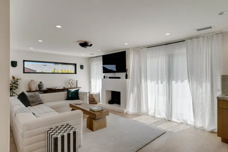 Living room with a curved white sectional, plastered fireplace, clerestory window, and sheer floor-length curtains