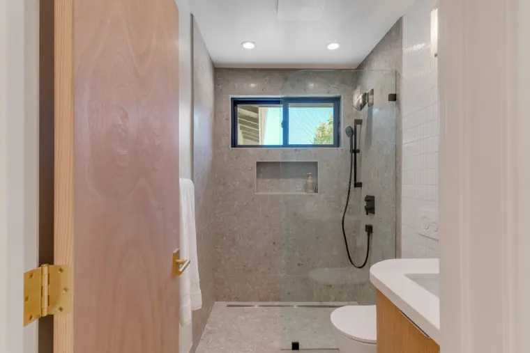 Bathroom with a speckled stone-tile walk-in shower, black shower fixtures, niche, wall-hung toilet, and a wood-grain door
