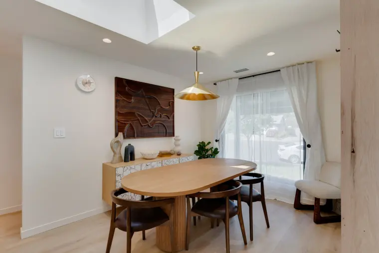 Dining area with an oval wood table beneath a brass pendant, a slatted wood wall, and garden doors