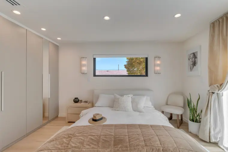 Bedroom with a clerestory window, wall sconces, full-height closets, and pale oak floors