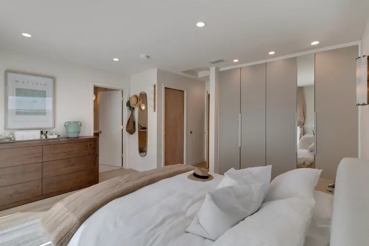 Bedroom with a wood dresser, full-height white closets, and soft layered bedding