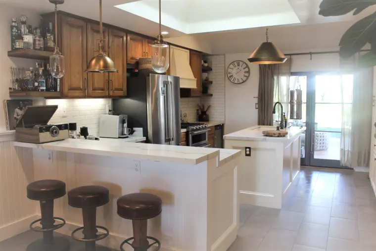 Kitchen with wood upper cabinets, white paneled peninsula, brass pendants, and French doors