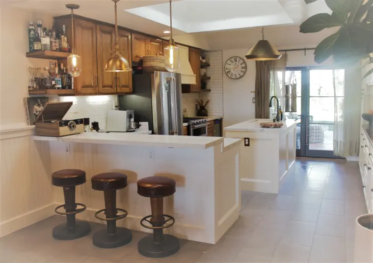 White peninsula with bar stools, open wood shelves, and a white subway tile backsplash