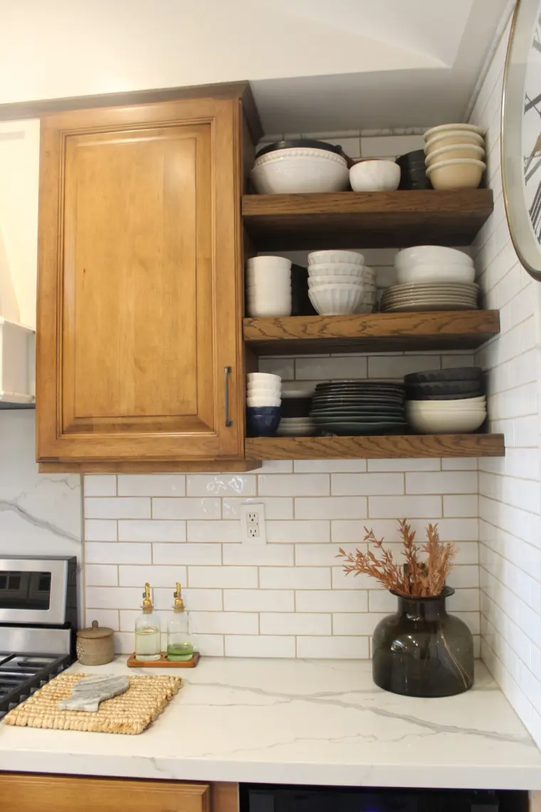 Wood cabinet and open shelves over a white marble-look counter and subway tile