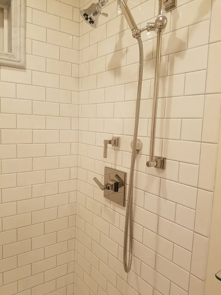Shower with white subway tile and a nickel slide bar with a handheld sprayer