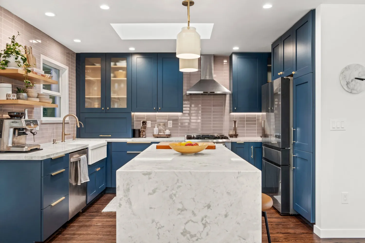 Navy shaker kitchen with a white waterfall island, skylight, glass-front upper cabinets, and a stainless range under a chimney hood