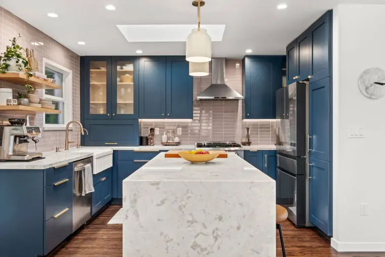 Navy shaker kitchen with a white waterfall island, skylight, glass-front upper cabinets, and a stainless range under a chimney hood