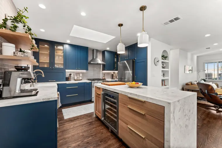 Waterfall island with warm wood drawer fronts and a wine fridge, navy cabinets and open wood shelving behind
