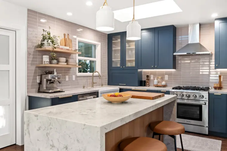 Quartz waterfall island with leather counter stools, navy cabinetry, and a professional-style range
