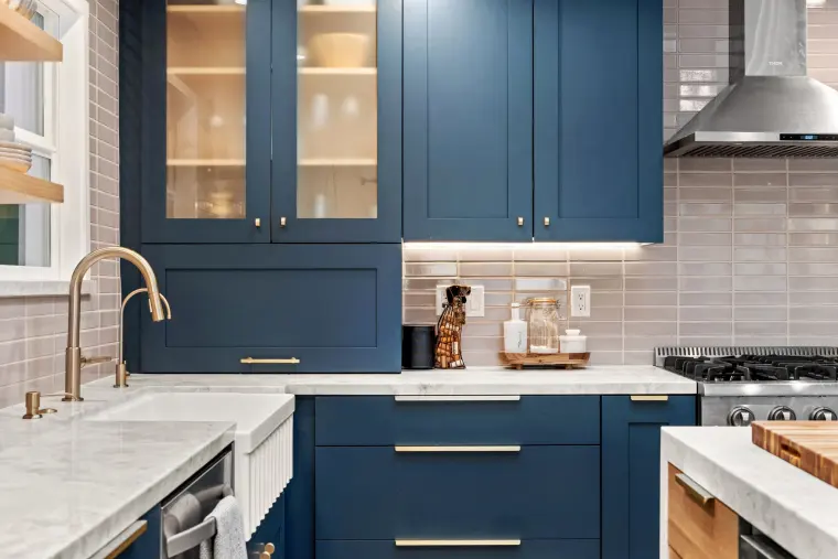 Navy lower cabinets with brass pulls beneath the farmhouse sink and quartz counters