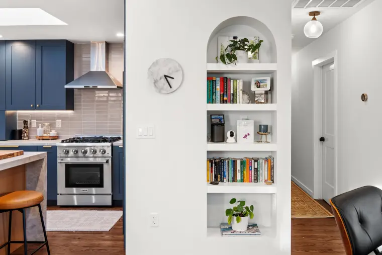 Stainless range with a chimney hood beside an arched built-in bookshelf niche