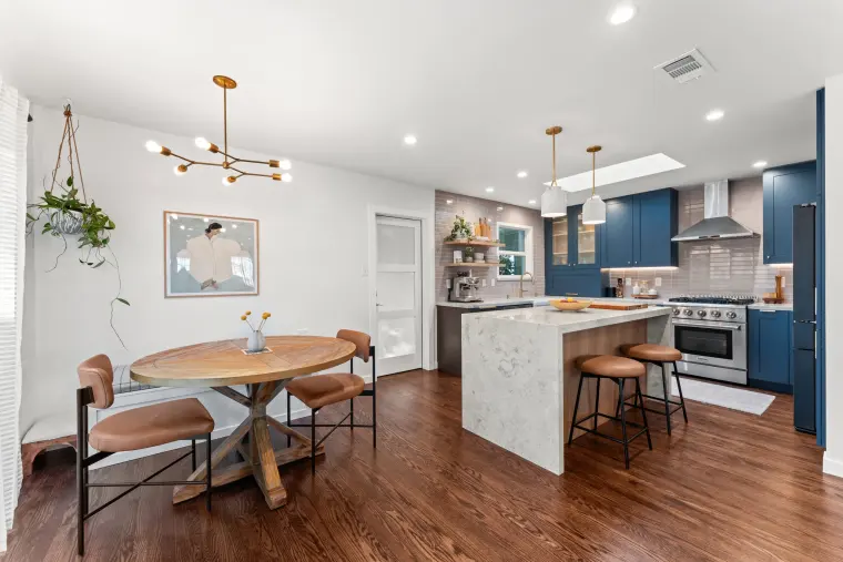 Open dining and kitchen area with a round wood table, brass sputnik chandelier, and a waterfall island with leather stools