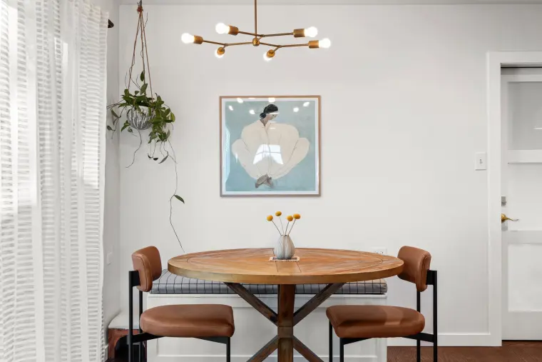 Dining nook with a round wood table, leather chairs, and a hanging plant by the window