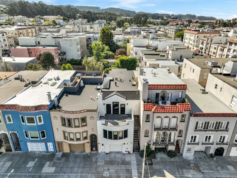 Aerial drone view of the renovated three-story rowhouse with a white and black facade and roof deck among neighboring San Francisco homes