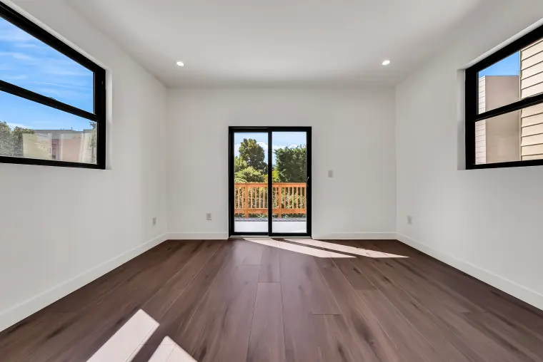 Bedroom with two black-framed windows flanking a sliding glass door to a wood deck, and wood flooring