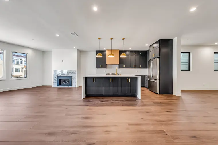 Open living area facing a kitchen with black shaker cabinets, brass dome pendants, a waterfall quartz island, and a marble-surround fireplace