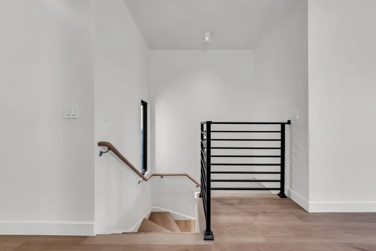 Stair landing with a black horizontal metal railing, a wood handrail, white walls, and light oak flooring