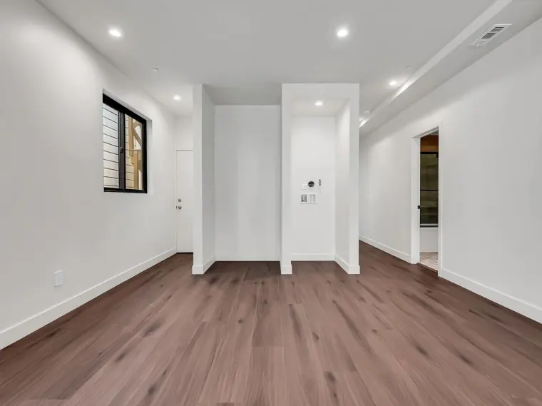 Empty finished hallway with white walls, wood flooring, built-in nook, and doorway views into a bathroom and closet